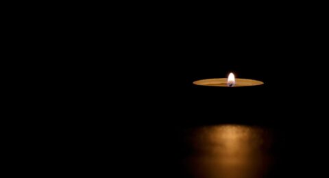 Lit tin candle in the dark conveying memorial, death, hope or darkness